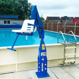 輪椅王 室外游泳池旁邊有一台藍色固定泳池升降機 F100，旨在幫助人們進出水面。池畔還設有金屬梯。