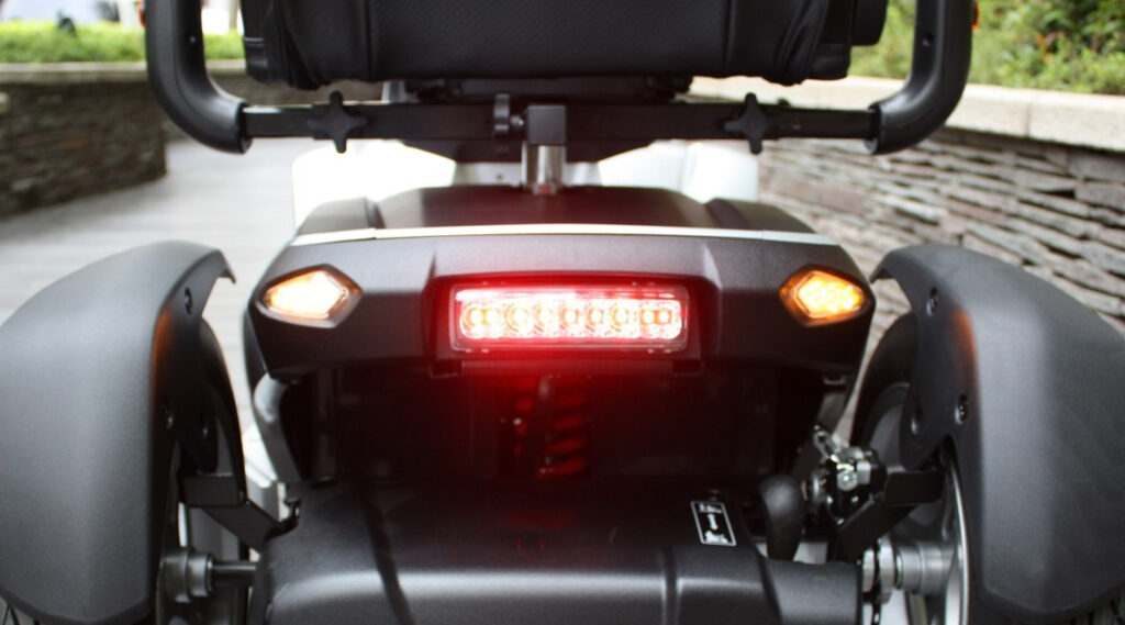 輪椅王 電動輪椅後方的特寫，顯示其紅色煞車燈和兩側較小的琥珀色燈。
