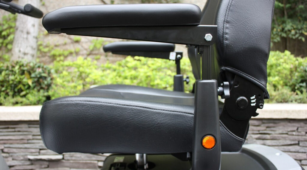 輪椅王 戶外花園中配有帶扶手和可調節靠背的黑色軟墊椅子，旁邊是 Merits WCS940 大型四輪代步車/輪椅。