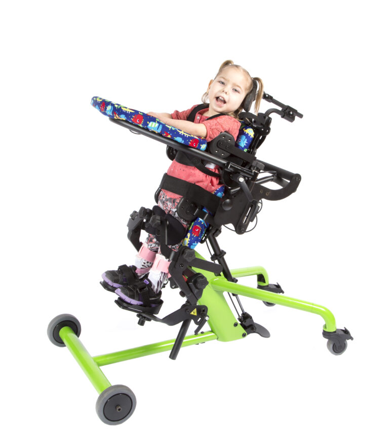 【輪椅王】 一個微笑的綁著辮子的孩子被固定在一個帶有綠色底座和黑色支撐的站立框架中。孩子穿著紅色襯衫和圖案緊身褲，舒適地站在兒童輪椅 PT50001-1 Bantam Extra Small 中。孩子麵前的托盤上裝飾著色彩繽紛的圖案，設備配有輪子，方便移動。