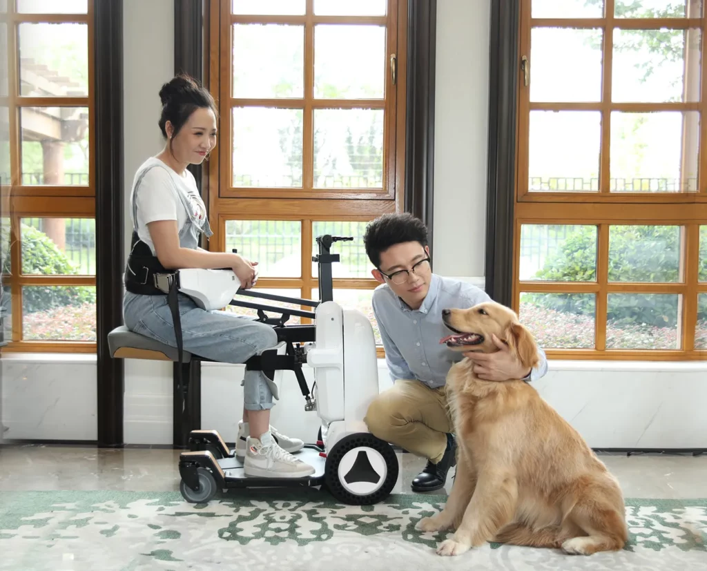 【輪椅王】 在一間裝有大木窗的房間裡，一名坐在 XZ-Droid Smart 輪椅上的女士和一名跪在她旁邊的男子撫摸著一隻金毛獵犬。