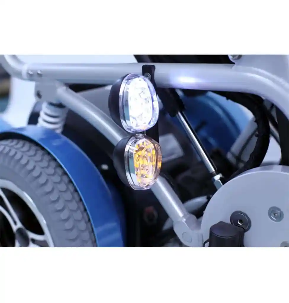 【輪椅王】 KARMAN XO505 垂直電動輪椅的後輪和車架的特寫，附有兩盞燈：一盞白燈和一盞琥珀色燈，均亮起。